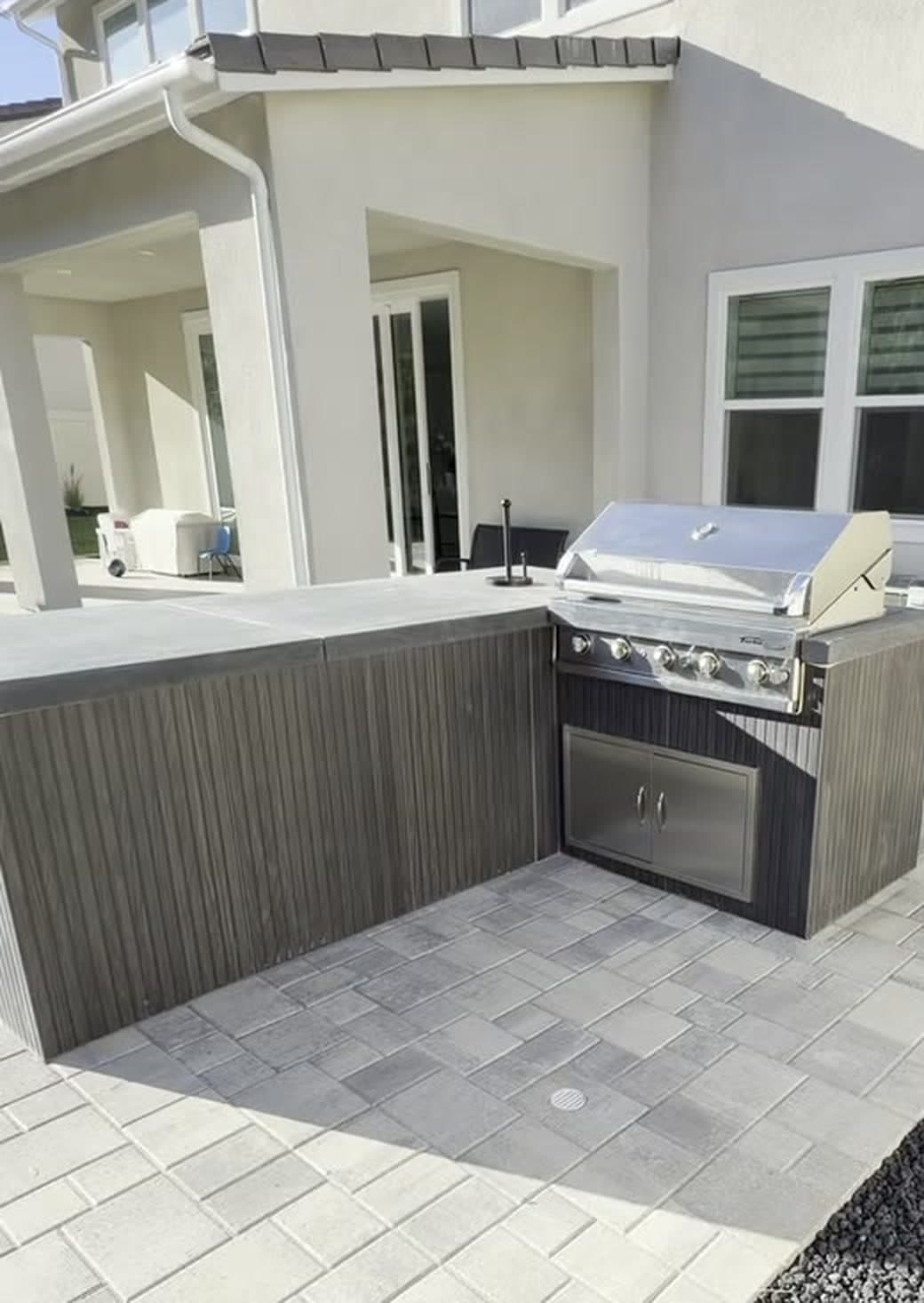 Completed backyard outdoor kitchen, covered patio, and pavers in daylight